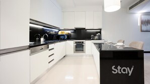 A modern kitchen with white cabinetry, a black countertop, and a dining area with a black table and chairs. - Chic 1BR at JW Marriott Hotel, Dubai Marina (Dubai Marina)