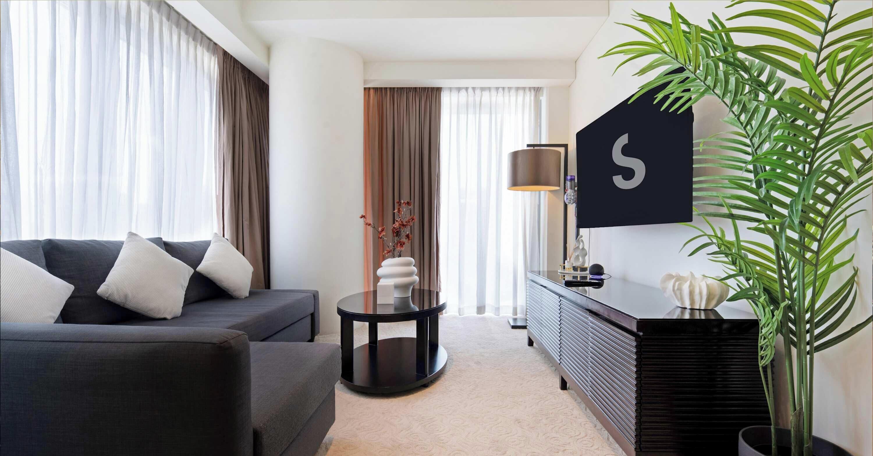A modern living room with a sofa, a side table, a lamp, and a potted plant.