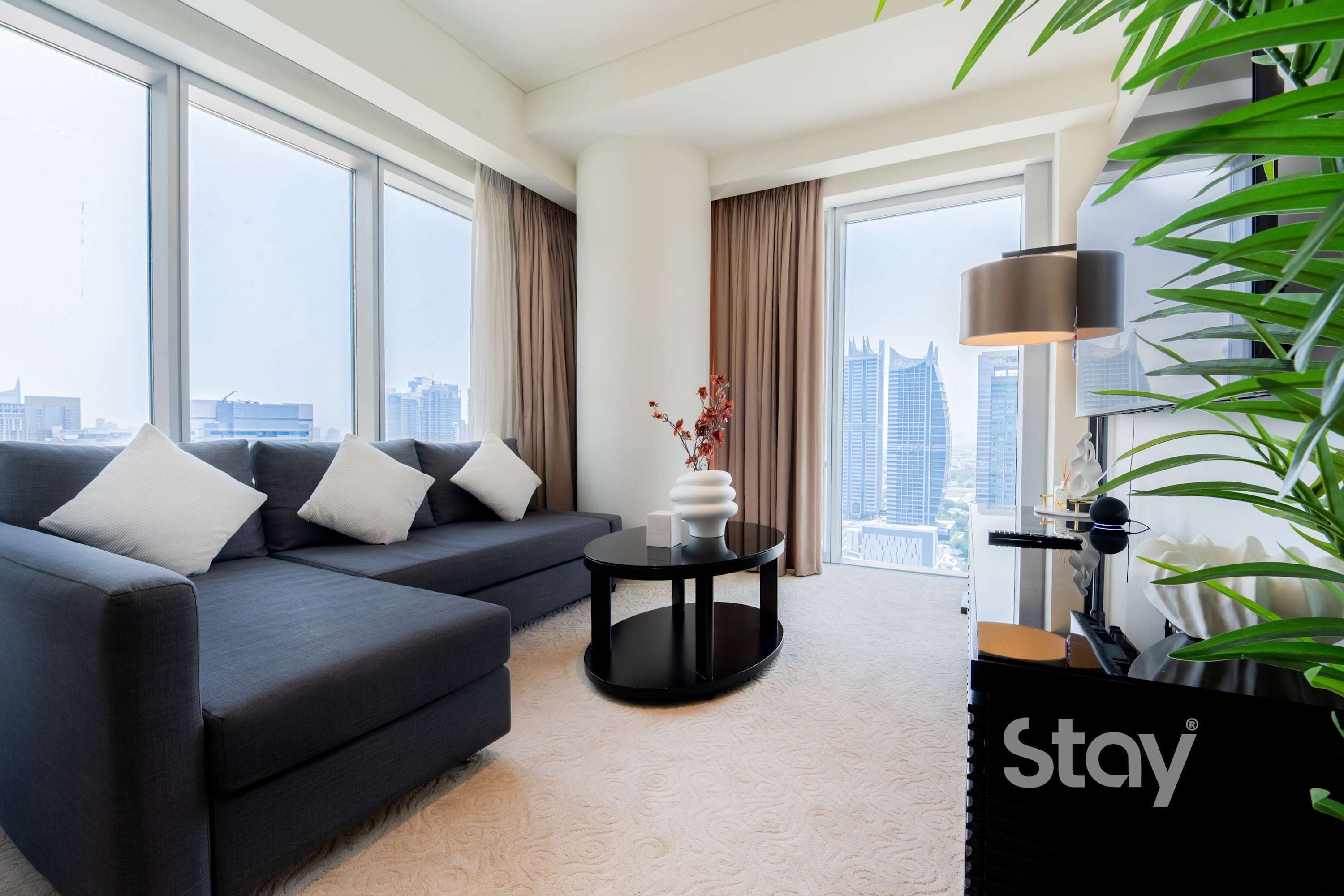 Une chambre d’hôtel moderne avec un canapé, une petite table, une lampe et une vue sur le paysage urbain.