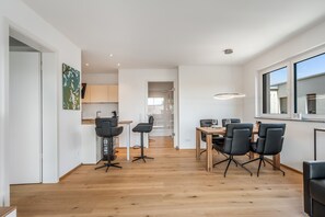 A modern kitchen with wooden flooring, a dining area with black chairs, and a large window. - "Berg und See" Vacation Rental - Enjoy a Modern Apartment with Panoramic Views of Lake Constance (Lindau (Bodensee))
