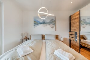 A modern bedroom with a large bed, a wooden wardrobe, and a painting of mountains. - "Berg und See" Vacation Rental - Enjoy a Modern Apartment with Panoramic Views of Lake Constance (Lindau (Bodensee))