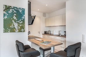 A modern kitchen with white cabinets, a wooden countertop, and a painting of white flowers on the wall. - "Berg und See" Vacation Rental - Enjoy a Modern Apartment with Panoramic Views of Lake Constance (Lindau (Bodensee))