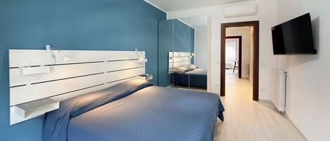 A modern bedroom with a large bed, bedside tables, a mirror, a TV, and a chandelier.