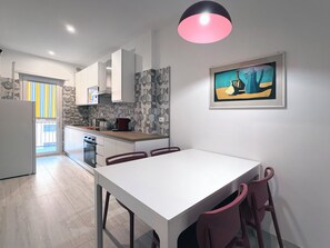 A modern kitchen with white cabinets, a dining table with chairs, and a painting on the wall. - 3Bed Flat Priv Parking Metro 4min Walk (Roma)