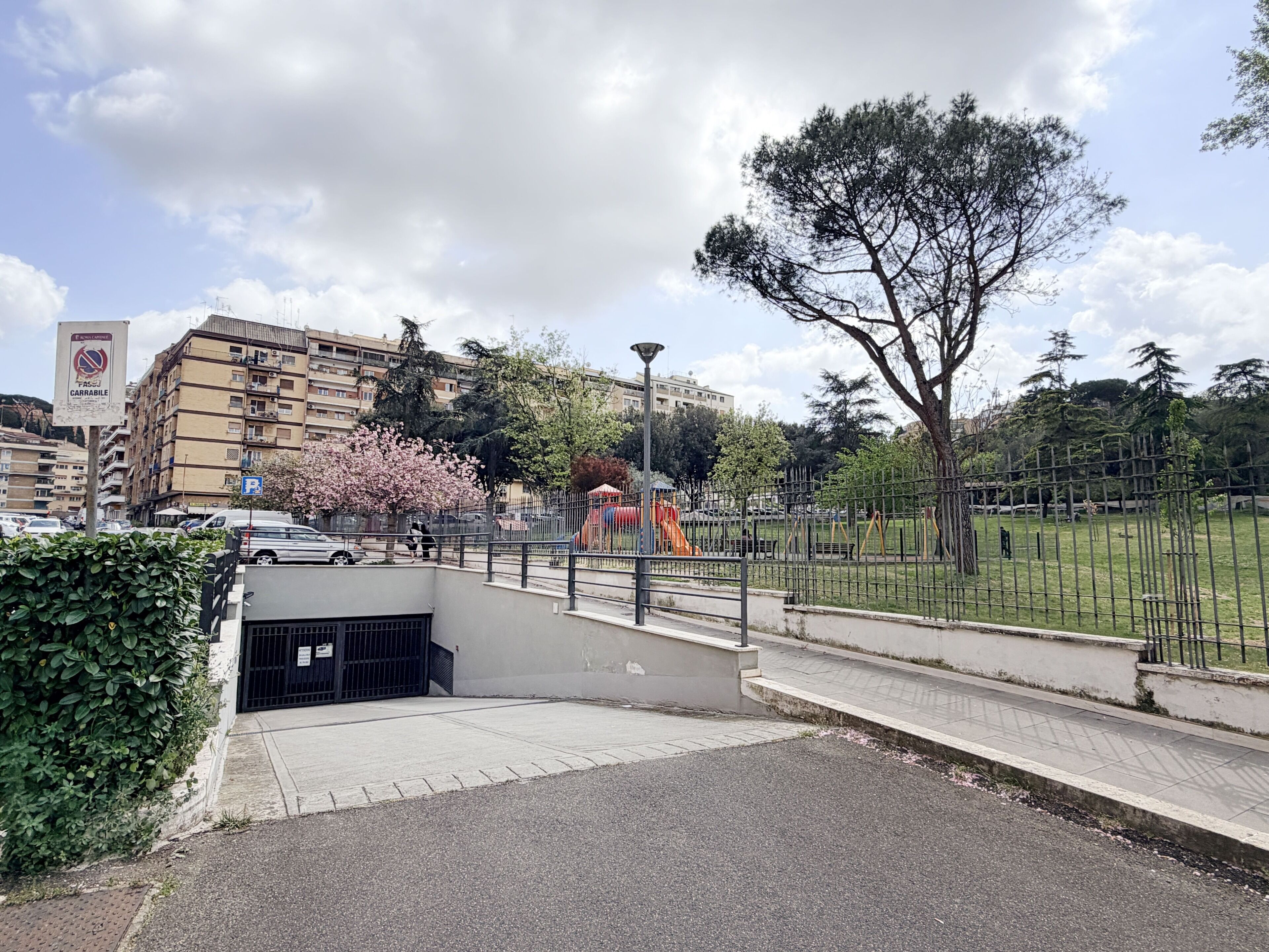 A parking area with a gated entrance, a playground with a slide, and a large tree.