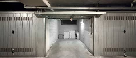 A parking garage with concrete walls and metal doors, featuring a central walkway and a row of storage units.