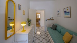 A room with a large mirror, a green sofa, a small table with a lamp, and a hallway leading to a kitchen. - Casa Albachiara Waterfront Just Steps From the Beach (Praiano)