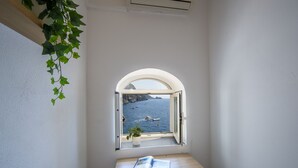A small room with a window overlooking a body of water and boats, a table with a book, and a potted plant. - Casa Albachiara Waterfront Just Steps From the Beach (Praiano)