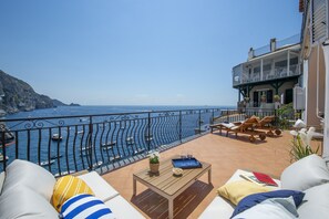 Eine Terrasse mit Meerblick, Liegestühle, ein Tisch mit Getränken und ein Gebäude mit Balkonen.