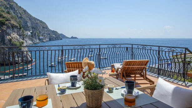 A terrace with a view of the sea, wooden furniture, and a table set for a meal. - Casa Albachiara Waterfront Just Steps From the Beach (Praiano)