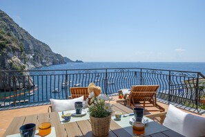 Eine Terrasse mit Meerblick, Holzmöbel und einem Tisch, gedeckt für eine Mahlzeit.