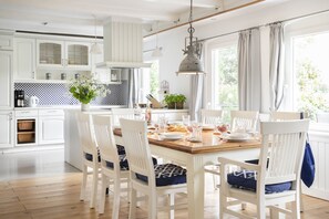 Eine helle Küche mit weißen Schränken, einem Holzespeisetisch für vier Personen und einem großen Fenster mit Vorhängen.