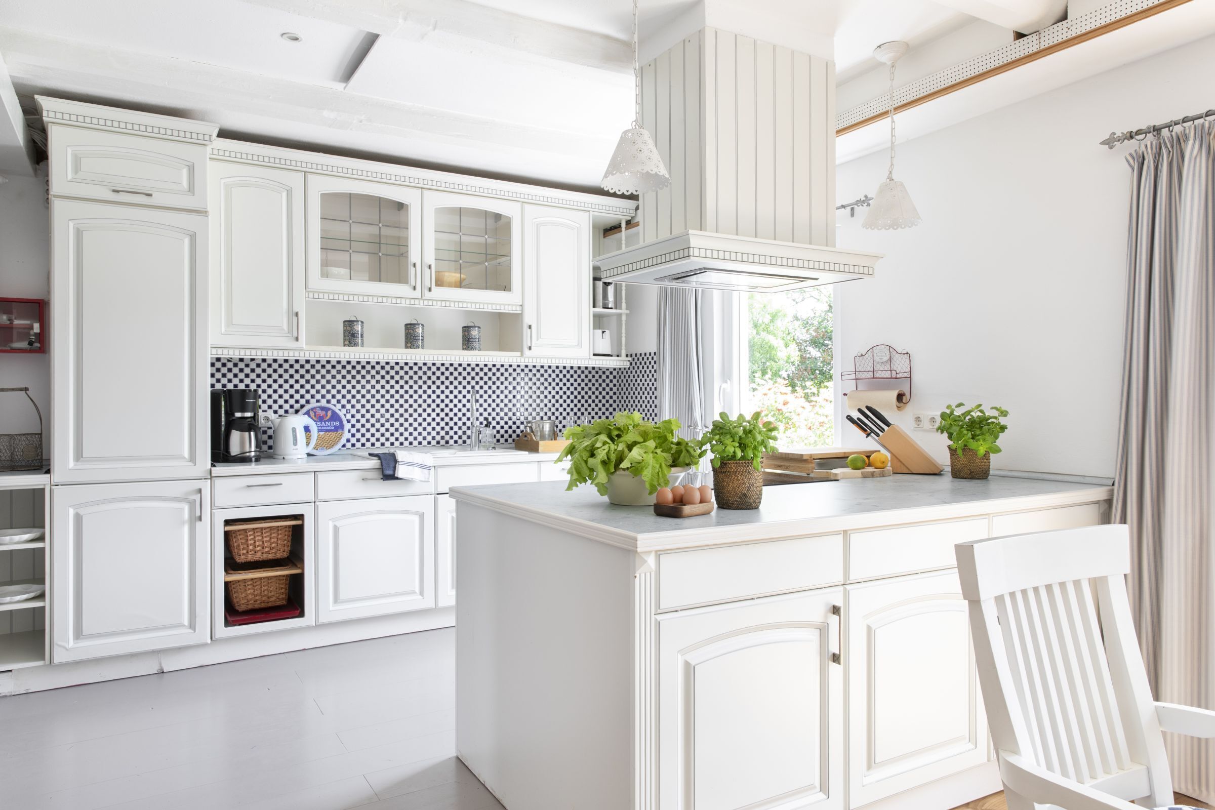 Une cuisine moderne avec des meubles blancs, un îlot central et des luminaires suspendus.
