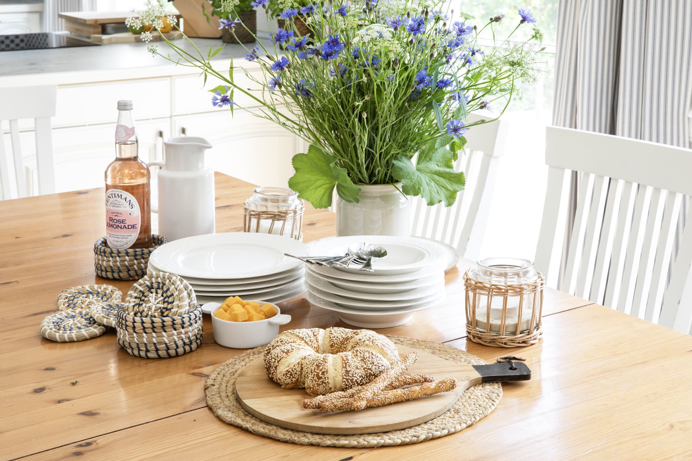 A dining table with plates, a bottle, a jar, a basket, and a loaf of bread.