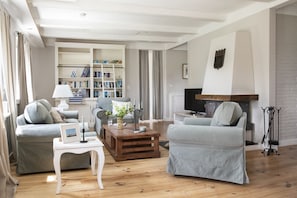Ein Wohnzimmer mit zwei grauen Sofas, einem Holztisch, einem Bücherregal, einem Kamin und einem Fernseher.