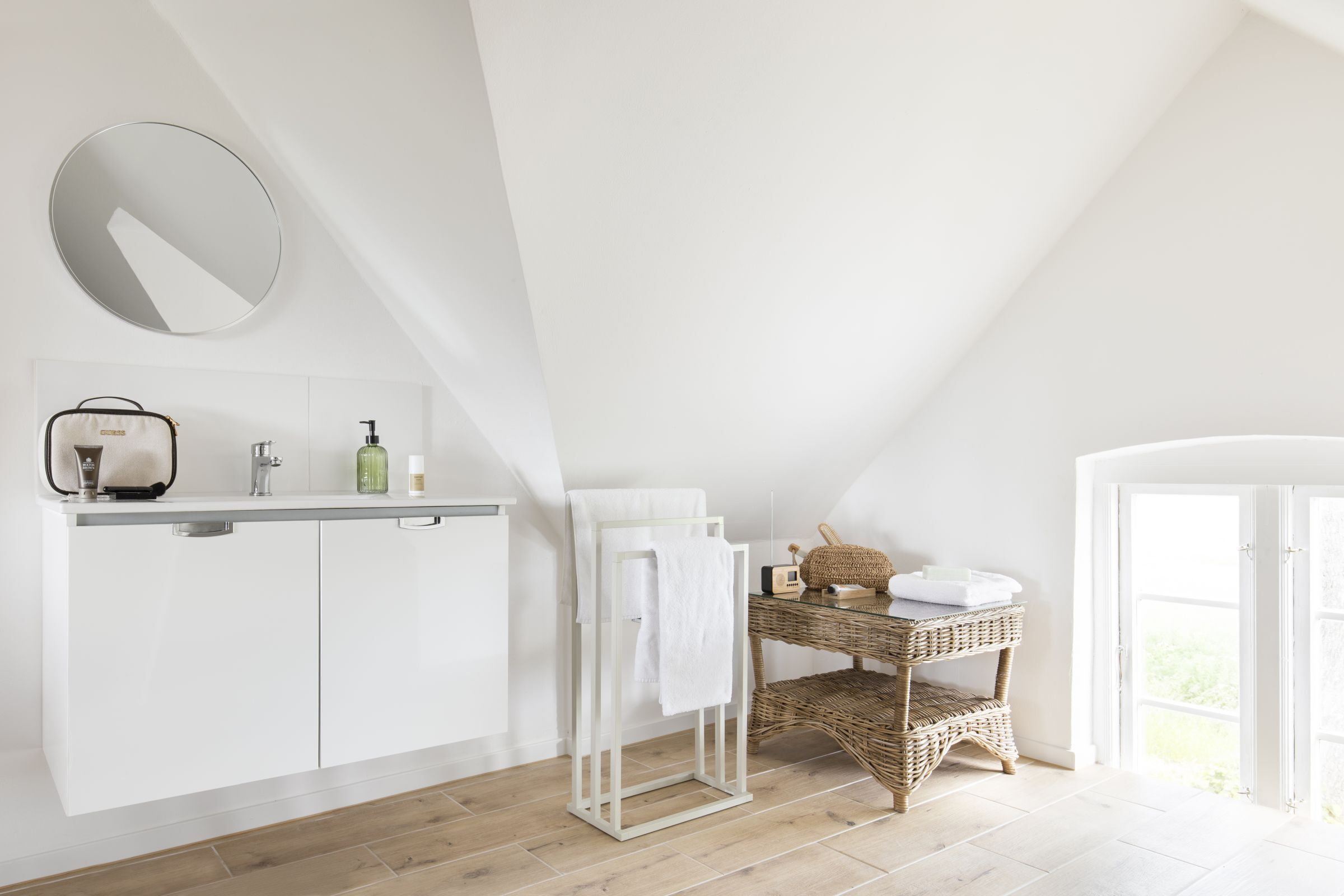Ein modernes Badezimmer mit schräger Decke, einem weißen Waschtisch, einem Korbtisch und einem großen Spiegel.