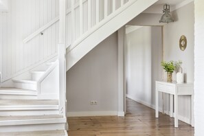 Eine Treppe führt zu einer Zwischenebene mit Holzboden, einem weißen Konsolentisch mit Pflanze und einem Spiegel an der Wand.