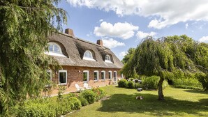 Ein traditionelles Backsteinhaus mit einem strohgedeckten Dach, umgeben von einem gepflegten Garten und Bäumen.