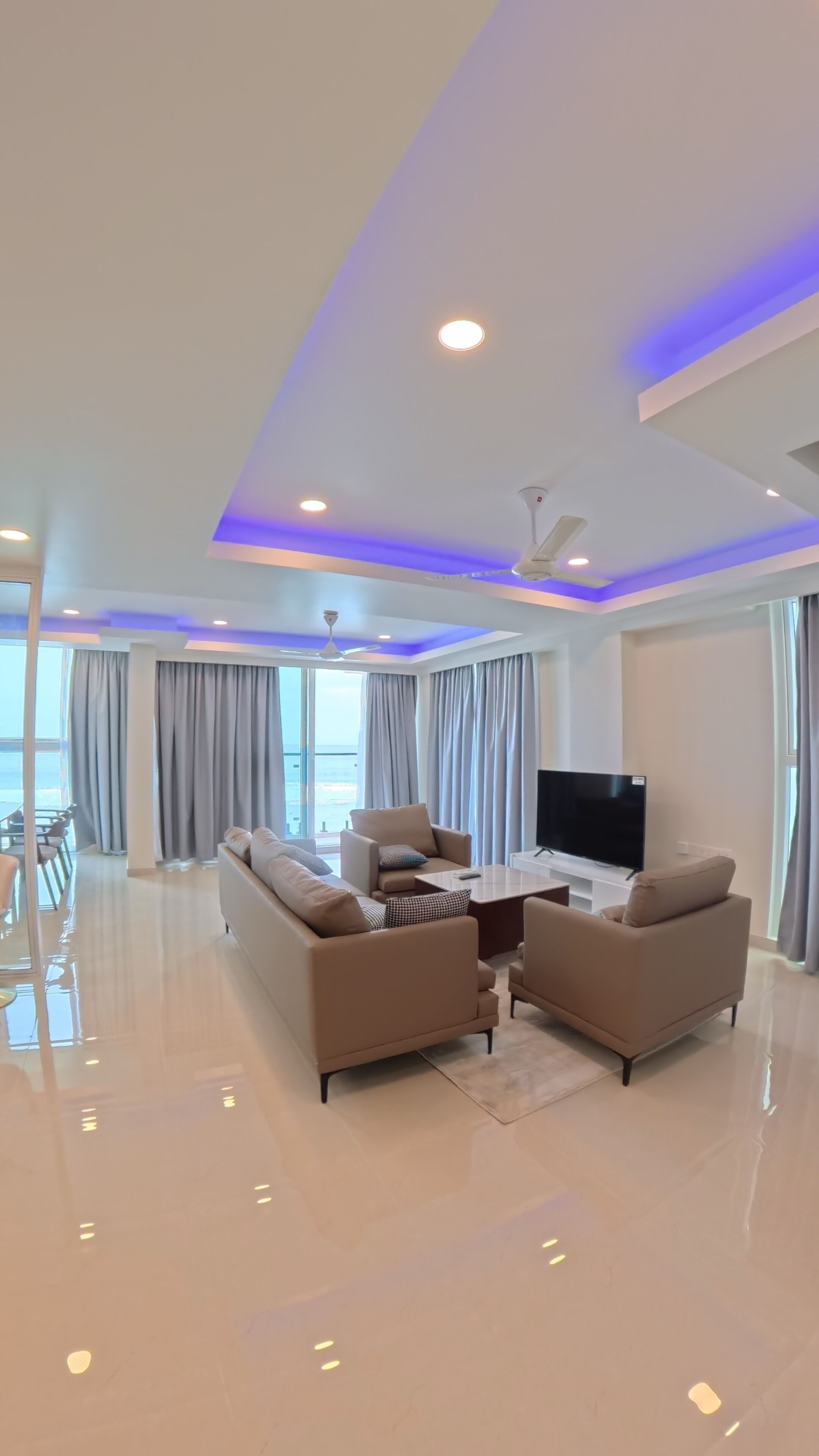 A modern living room with a sofa set, a flat-screen TV, and a ceiling fan.