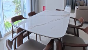 Ett modernt matområde med ett vitt marmorbord och trästolar, stora fönster med gardiner och en takfläkt.