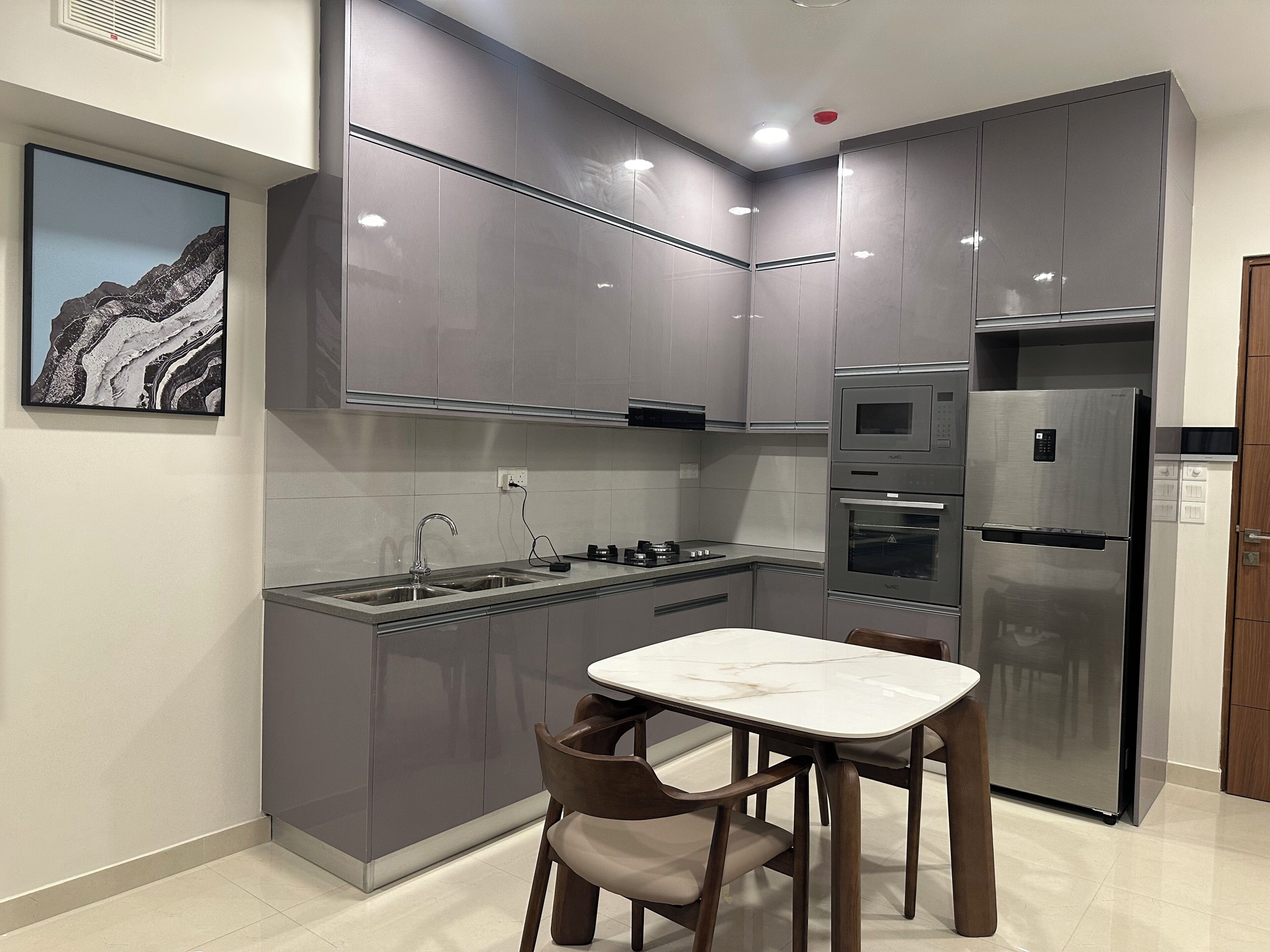 A modern kitchen with grey cabinets, a stainless steel refrigerator, a built-in oven, and a marble countertop.