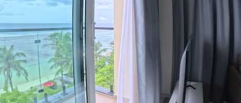 Una habitación de hotel moderna con un ventanal grande, un televisor de pantalla plana y un balcón con vistas al océano.