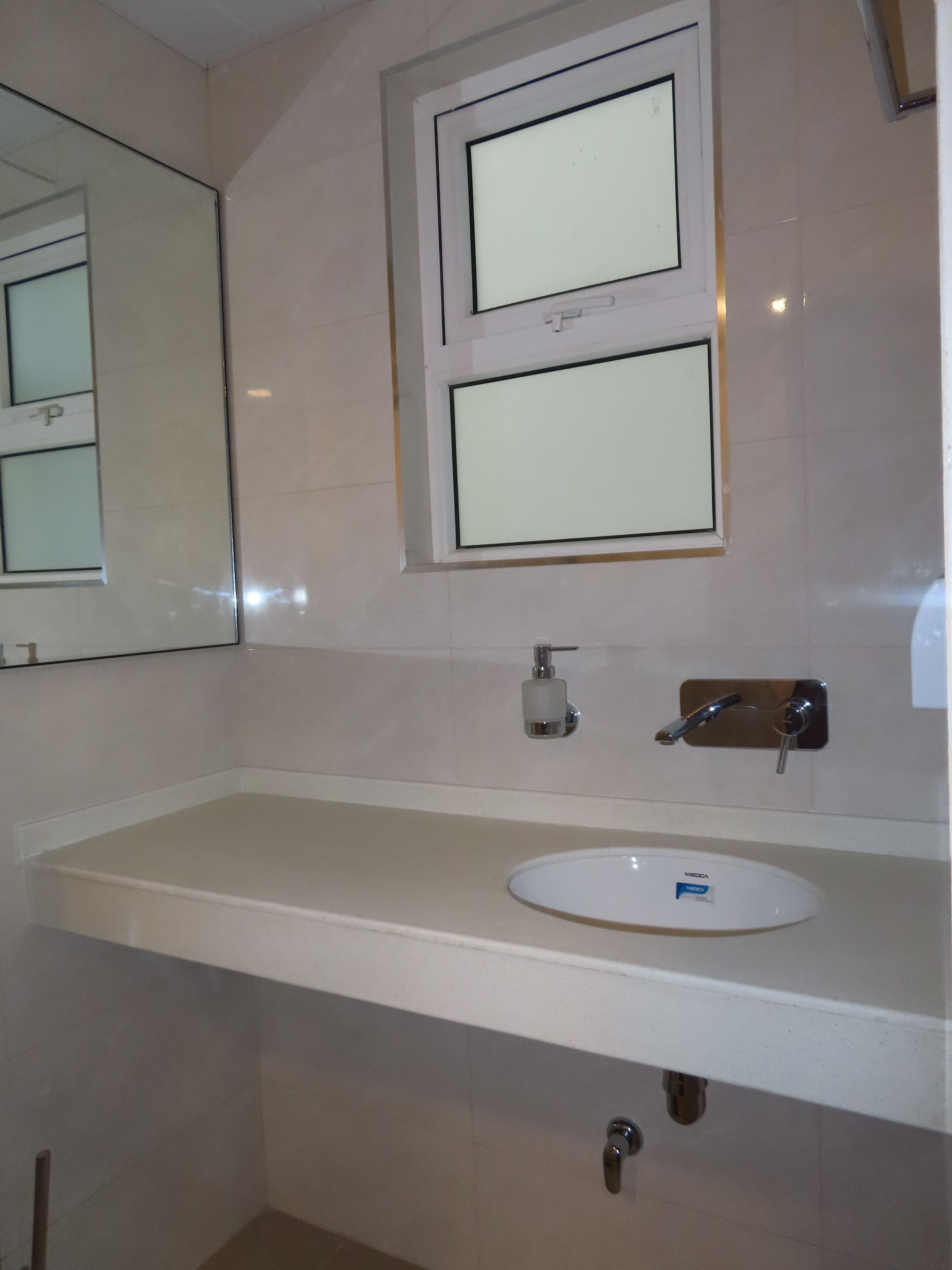 A bathroom with a white sink, a mirror, and a soap dispenser.
