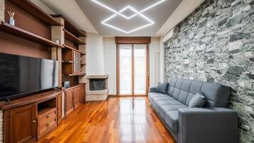 Een woonkamer met een open haard, houten vloeren, een grijze bank en een stenen muur.