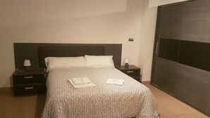 A hotel room with a bed, two bedside tables, a nightstand, a wardrobe, and a wall-mounted control panel. - Hotel Avenida del Sotillo (La Lastrilla)