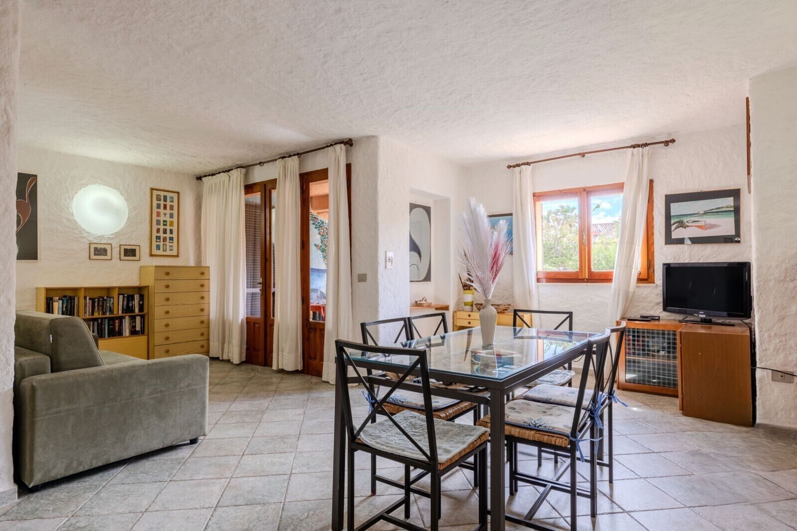 A spacious living area with a dining table, chairs, a sofa, a television, and a bookshelf.