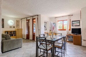 A spacious living area with a dining table, chairs, a sofa, a television, and a bookshelf. - Appartamento delle Margherite by Wonderful Italy (Budoni)