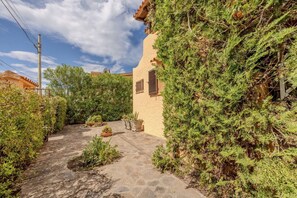 A stone pathway leading to a building with a tiled roof, surrounded by dense greenery and a clear sky. - Appartamento delle Margherite by Wonderful Italy (Budoni)
