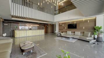 A modern hotel lobby with a reception desk, seating area, and a large TV screen.