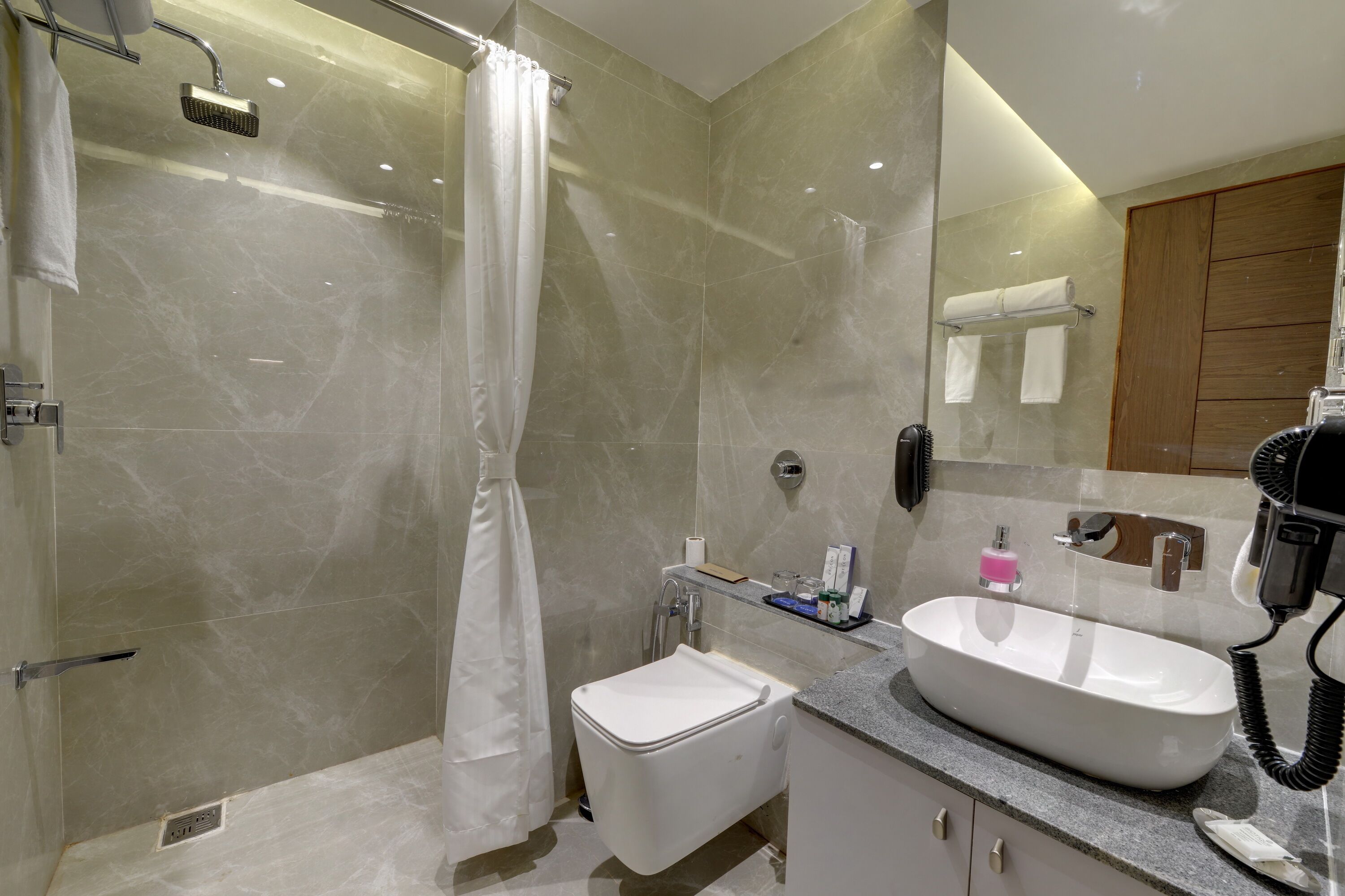 Une salle de bain moderne avec une douche à parois de verre, un lavabo blanc et un sèche-cheveux posé sur le comptoir.