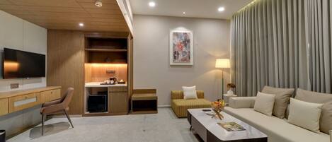 A modern living room with a flat-screen TV, a sofa, a coffee table, and a dining area with a small kitchen setup.