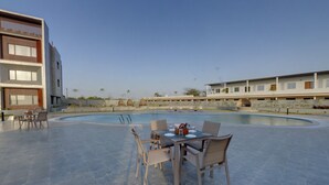 A pool area with a table and chairs, surrounded by buildings. - Desert Inn Beacon Greater Rann of Kutch (Bhuj)