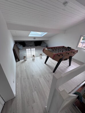 Une pièce avec une table de baby-foot, un lit avec des oreillers, une lucarne et une fenêtre.