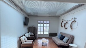 A spacious living area with a high ceiling, a sofa set, a wicker chair, a patterned rug, and a television mounted on the wall. - A traditional Landes-style house nestled between the ocean, the forests, and the lakes (Ondres)