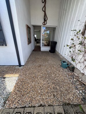 Un chemin menant à une porte, une corde suspendue, une poubelle et une plante en pot.