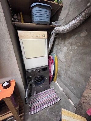 Un espace réduit dédié à la buanderie, comprenant un lave-linge, un étendoir et une petite étagère avec des bacs de rangement.