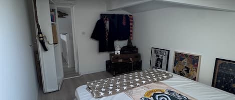 Quarto com claraboia, cama com colcha estampada, guarda-roupa e uma pequena mesa com livros.