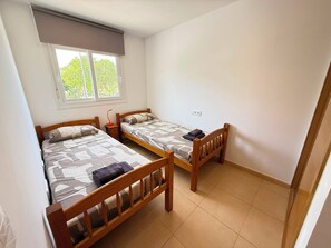 A small, clean room with two wooden beds, a window with a view of greenery, and a tiled floor. - Alhama County - Apartment 186 N3 (MC)