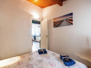 Um quarto com uma cama, uma pintura de um cais e vista para a cozinha.