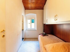 A narrow hallway leading to a bedroom with a wooden ceiling, a window with blinds, and a bed with a rolled-up blanket. - Apartment Lily by Interhome (Imperia)