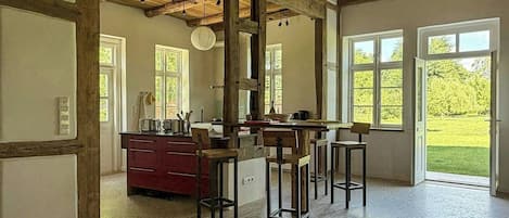 Uma cozinha espaçosa com vigas de madeira, um armário vermelho e vista para um jardim através de grandes janelas.