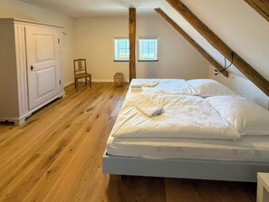 A bedroom with a large bed, a wardrobe, a chair, and two windows.