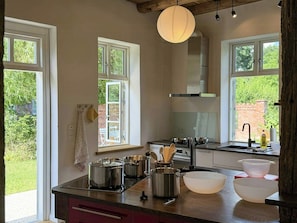 A kitchen with large windows, a gas stove, stainless steel pots, and a wooden countertop.