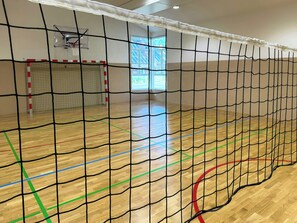 An indoor sports facility with a basketball court, a netted area, and a goal.