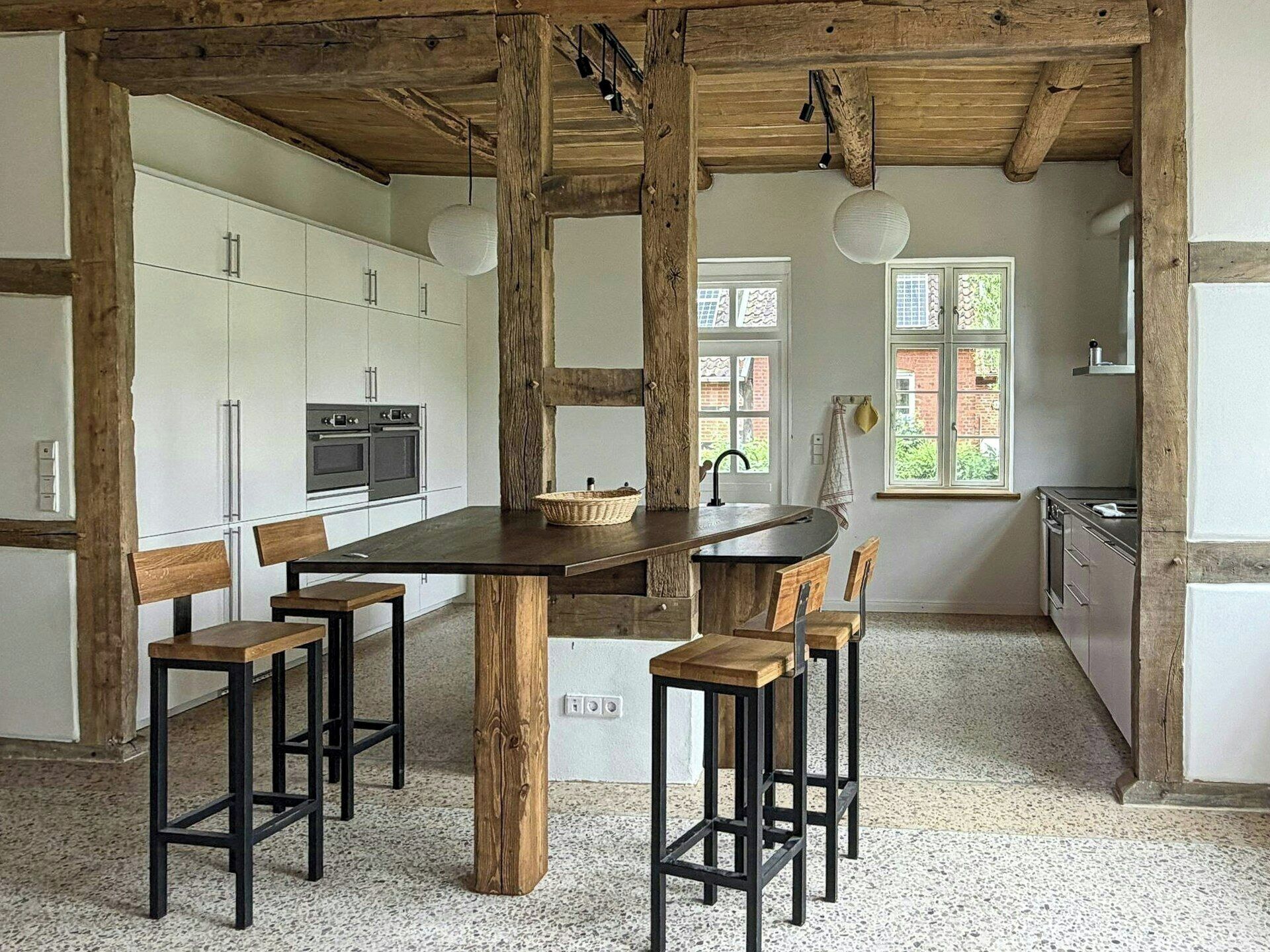 A kitchen with a central island, wooden stools, and a rustic ceiling.