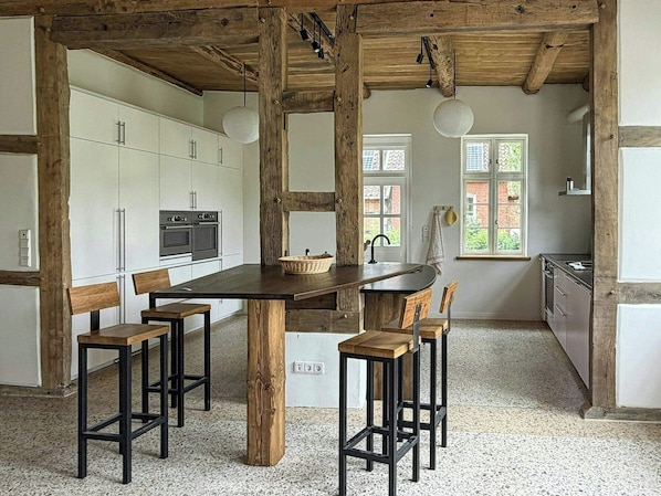 A kitchen with a central island, wooden stools, and a rustic ceiling.